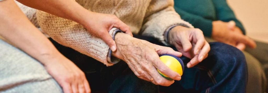 Nursing Home Staff Holding older persons hand while the older man holds a stress ball.