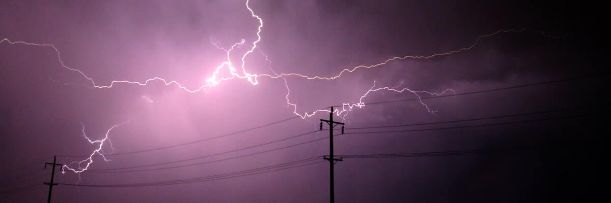 Lightning flashing against a backdrop of purple sky and electricity poles