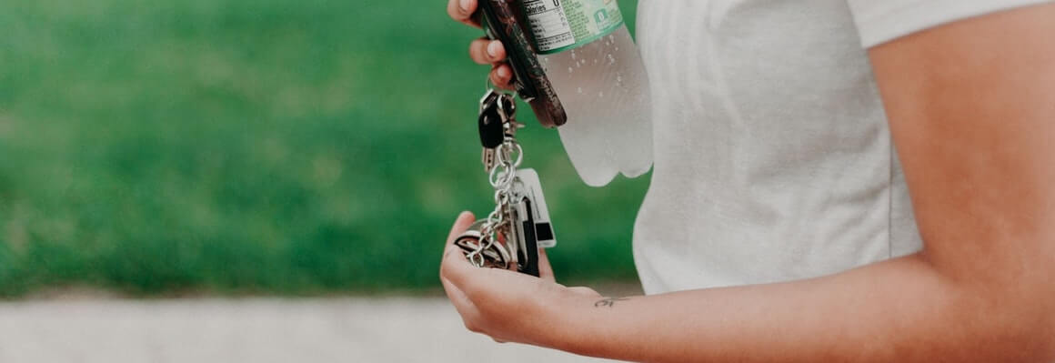 woman wearing white tshirt holding leased car keys, her phone, and a bottle of water. Set against a grass field.